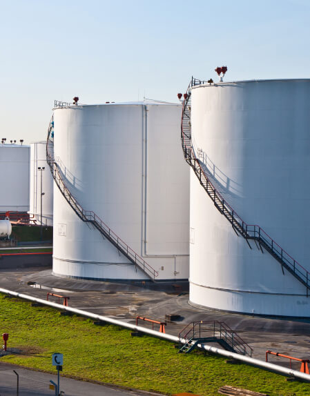 White cylindrical oil/chemical storage tanks with spiral staircases under a blue sky.